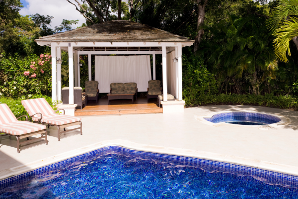 A poolside cabana with lounge chairs and a covered seating area surrounded by lush greenery.